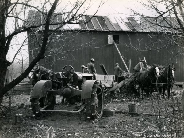 Farmers use a 6-roll husker shredder and a Farmall Regular tractor outside a barn on the farm of Will Rasque.