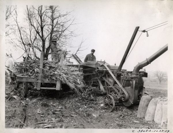 Two men work on the Will Rasque farm using a horse-drawn wagon and a six-roll husker-shredder.