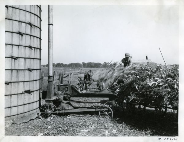 Farmer B.H. Zimmick uses a Farmall tractor and a Number 12 ensilage cutter near a silo.