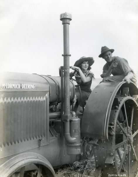 A woman, possibly actress Mary Duncan, sits behind the wheel of a McCormick-Deering tractor while a man stands beside her on the set of the Fox Film production "Our Daily Bread".