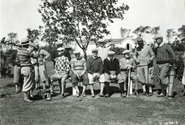 A group of male golfers are sitting and standing while posing for a portrait at an International Harvester employee picnic.