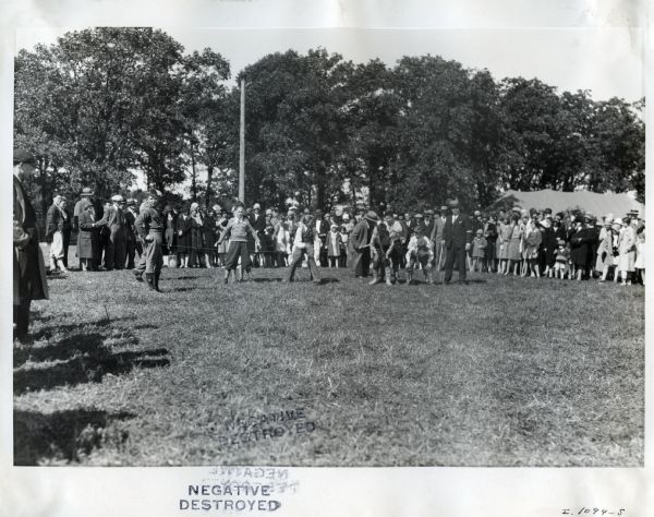 Boys line up for a race or game at an International Harvester employee picnic while a crowd forms to watch.