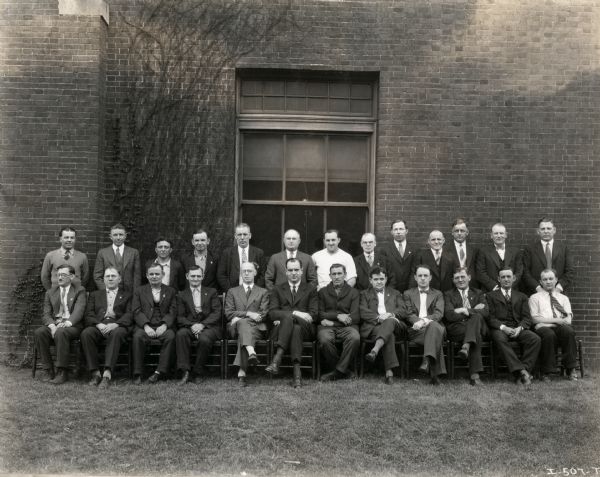 The men of the McCormick Works Council posing in front of the brick wall of a building for a group portrait.