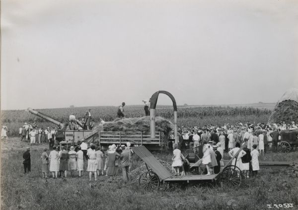 A group of spectators watching a threshing demonstration with wagons and a McCormick-Deering All-Steel Thresher.