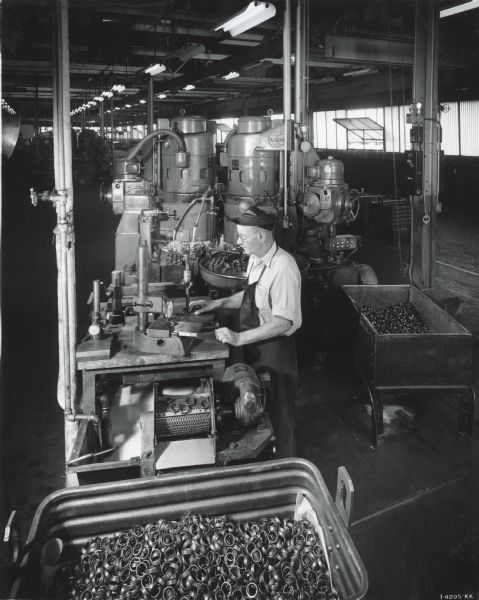 A factory worker at West Pullman Works stands behind a counter surrounded by metal pieces in the ball bearing plant.