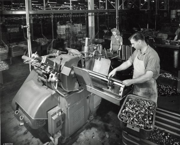 A male and a female factory worker operating machines in the ball bearing plant at West Pullman Works.