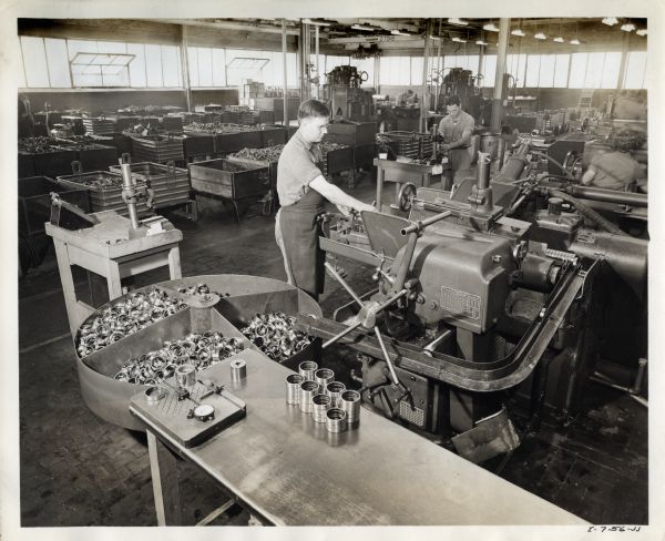 A factory worker at West Pullman Works uses a centerless grinder in the ball bearing department. A man and woman work in the background.