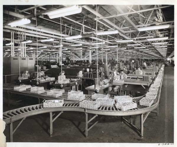 Female factory workers stand at tables behind an assembly line in the ball bearing department at West Pullman Works.