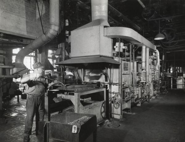 A man wearing protective gloves is shoveling metal pieces into a radiant tube clean hardening furnace at West Pullman Works.