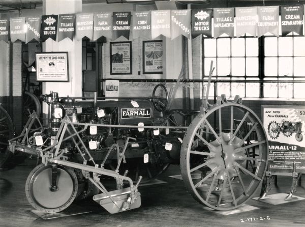 A Farmall-12 tractor sits on display underneath a string of banners, possibly at McCormick Works. A sign reading: "See This New Farmall" stands next to the tractor.