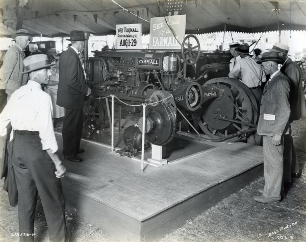 Men gather to look at a Farmall Regular tractor on display at the Indiana State Fair. The sign on top of the tractor reads: "4021 Farmall in use in Indiana up to Aug 1-29" and "See the Inside of the Farmall."
