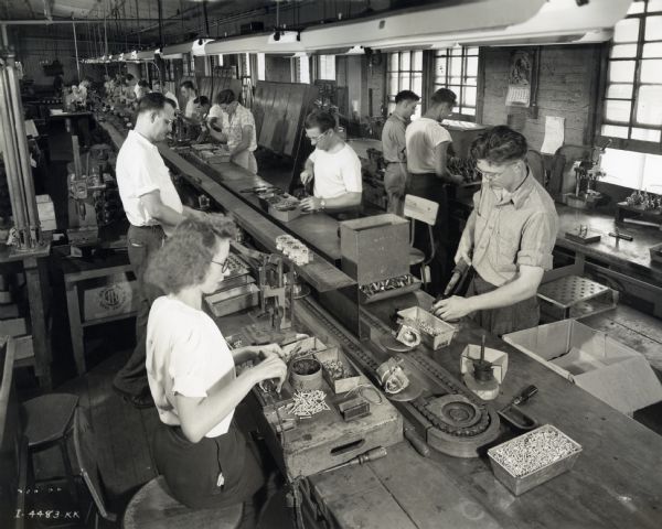 Male and female factory workers sitting and standing along an assembly line at West Pullman Works.