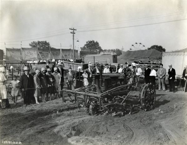 A crowd of spectators gathers around a Farmall Regular tractor on display at the Tri-State Fair.