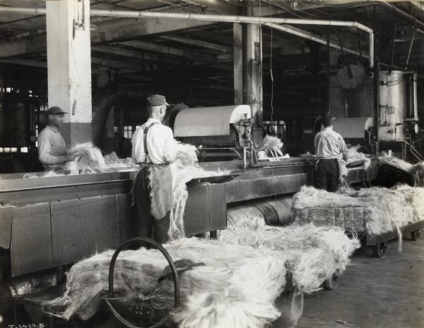 Factory workers handle twine piled on wheeled carts at Hamilton Twine Mills.