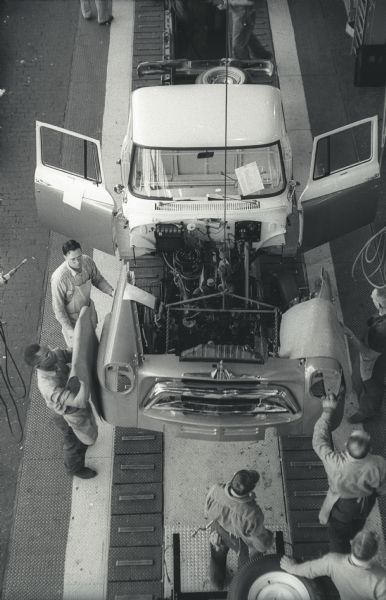 Elevated view of a five-man assembly team working on the body of an A-100 "Golden Jubilee" truck. The fender-grille unit is dropping through an opening in the trim line floor at International Harvester's Springfield Works.