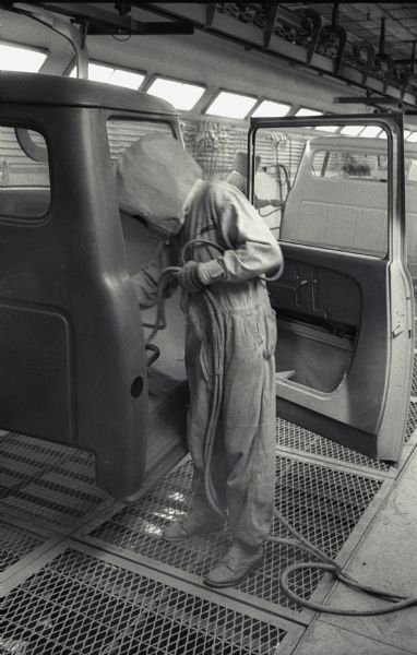 A factory worker wears a protective hood and face mask to paint the body of an International A-100 "Golden Jubilee" truck at International Harvester's Springfield Works.