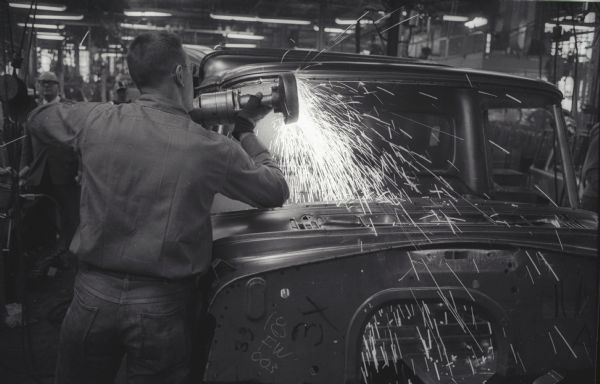 An factory worker causes sparks to fly by using a tool on the body of an A-100 "Golden Jubilee" model truck at International Harvester's Springfield Works.