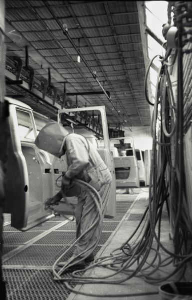 A factory worker in a protective suit and mask applies a coat of paint to an International A-100 "Golden Jubilee" truck cab at International Harvester's Springfield Works.