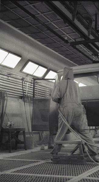 A factory worker dressed in a protective suit and mask applies a coat of paint to an International A-100 "Golden Jubilee" truck at International Harvester's Springfield Works.