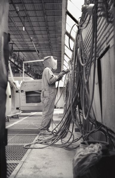 A factory worker selects a paint hose hanging from a wall to apply paint to an International A-100 "Golden Jubilee" truck at Springfield Works.