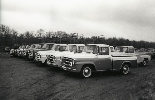 International trucks parked in a dirt lot and awaiting shipment, most likely near International Harvester's Springfield Works factory. Some of the trucks are A-100 "Golden Jubilee" models. The original caption reads: "First units off line were slated for April 4 announcement showings throughout U.S. From 4,200 to 33,000 lbs. GVW, new line includes 4x4's, 6x6's, Metros, panels, 3 new Travelalls, among others."