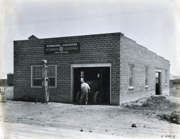 A man works on a tractor in the doorway of the Farmers Grain and Elevator Company, an International Harvester dealership and service station.
