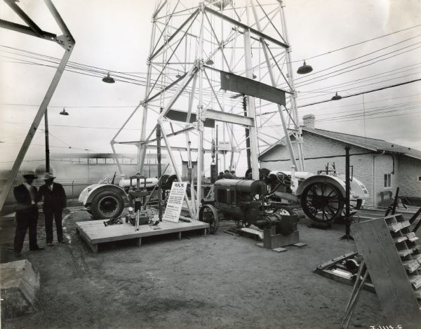Spectators look at agricultural machinery on display at the International Petroleum Exposition, including a white McCormick-Deering 15-30 tractor. The sign reads: "W.K.M. Fritts Type Dynamic Eliminator for Deep Oil Well Tubing; Prevents Tubing Movements, Prevents Tubing Collarware, Prevents Casing Ware, Prevents Lost Plunger Travel."