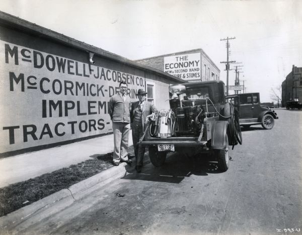 Two men stand next to a truck loaded with a cream separator outside the McDowell-Jacobsen Company, an International Harvester dealership.