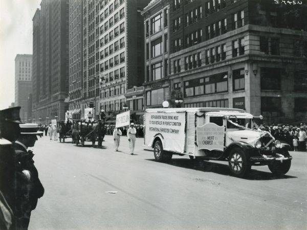 An International Harvester truck leads a line of marchers in the Meat Packers Parade. The parade is moving down a city street (possibly Michigan Avenue in Chicago). The sign on the truck reads: "Refrigerator trucks bring meat to your retailer in perfect condition" and "This keeps the meat cool, covered and sweet and meat is the cheapest in years."