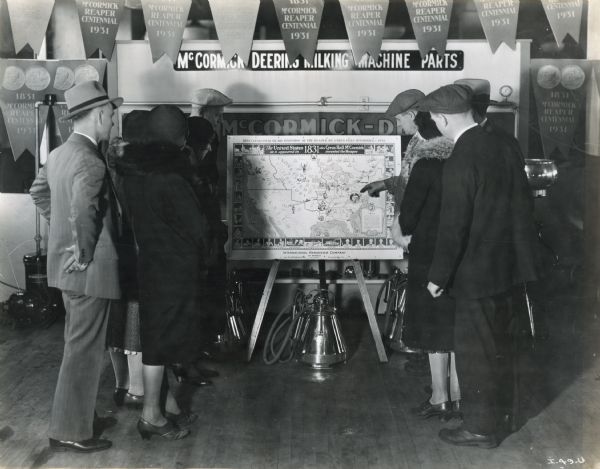 A group of people look at an 1831 United States map, part of a McCormick-Deering milking machine parts display.  The title on the map reads, "The United States as it appeared in 1831, the year Cyrus Hall McCormick invented the Reaper." The map was produced for the Reaper Centennial celebration.