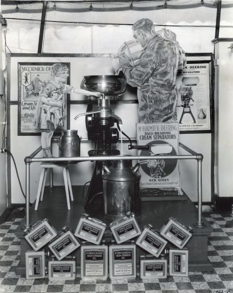 Cardboard cutouts of a man and a girl with a doll demonstrate the use of a cream separator. Cans of oil are arranged nearby. The display may have been part of the Wisconsin State Fair. The poster near the cream separator reads: "McCormick-Deering Ball-Bearing Cream Separators; Six Sizes; For One Cow or a Hundred."