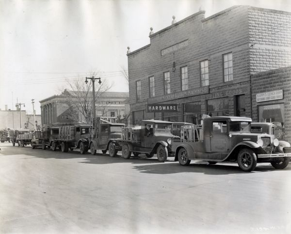 A line of several trucks in front of the Landaal Brothers Hardware store. Landaal Brothers was likely an International Harvester dealership. One of the trucks reads: "Lueck Implement Store; Ripon, Wis." The sign on the building to the right of the hardware store reads: "Happy's Lunch Room; Soft Drinks, Candy, Cigars, Tobacco."