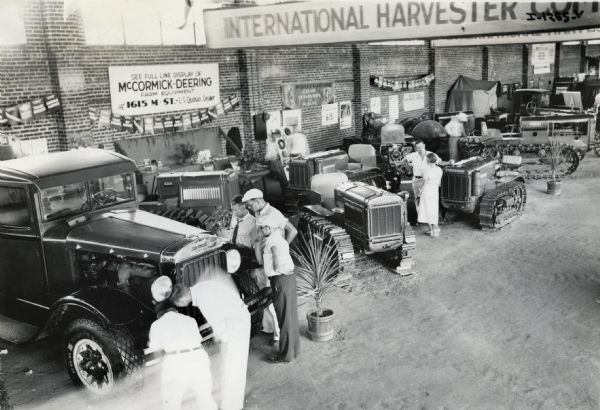 Exhibit-goers look at an International truck and a line of new crawler tractors (TracTracTors) arranged for International Harveser's display at the California State Fair. The sign on the wall reads: "See Full Line Display of McCormick-Deering Farm Equipment at 1615 M. St. - L.S. Quinan, Dealer." The original caption reads, "California State Fair Exhibit of I.H.C. newly-born line of tractors, September 2nd to 11th, 1932, Sacramento, California. Pictures were taken in the morning when the least crowd was expected. However it was practically impossible to clear the ground. Weak light intensity necessitated time exposure, and this resulted in phantom figures."