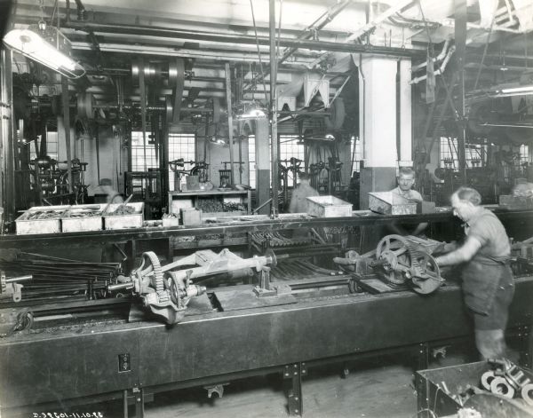 A factory worker works on part of a mower or grain binder while other men work in the background at International Harvester's McCormick Works.