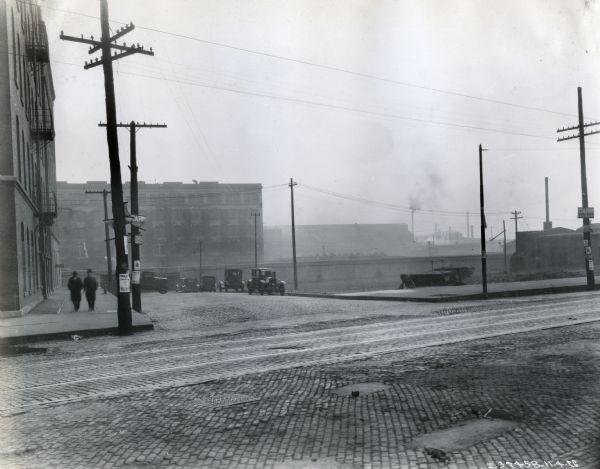 Two men wearing hats and overcoats walk along the sidewalk adjacent to a large building, possibly the McCormick Works factory. Signs on the electrical poles read, "Carr for Sheriff."