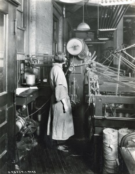 A female factory worker balling binder twine with a machine, most likely at International Harvester's McCormick Works Twine Mill.
