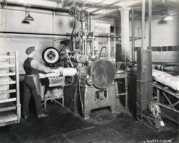 A man standing at a machine, in what is possibly the McCormick Works twine mill, handles bags, probably containing sisal to be made into twine.
