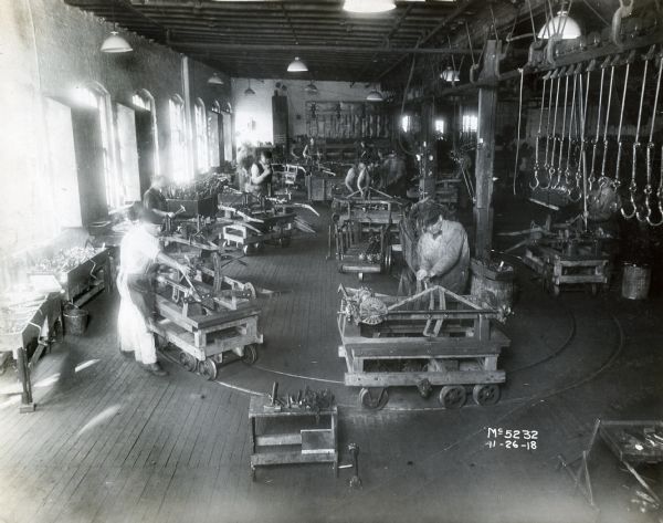 Factory workers tend to machines on wheeled carts at International Harvester's McCormick Works factory. The carts run along a track embedded in the floor.