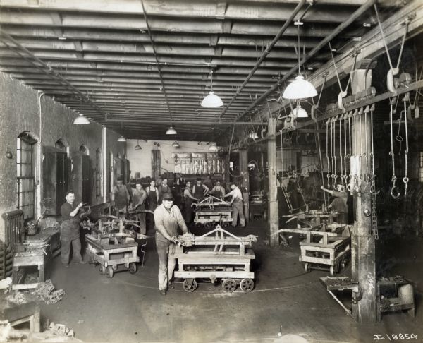 Factory workers assemble machines moving along a track on wooden carts at International Harvester's McCormick Works.