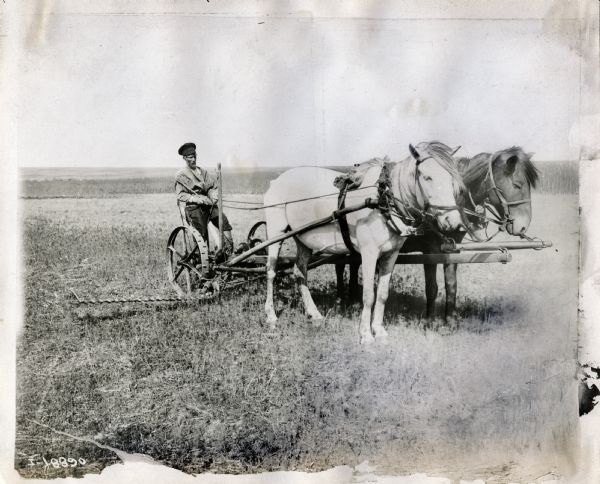 A farmer (possibly in Russia?) on a horse-drawn mower in a field.