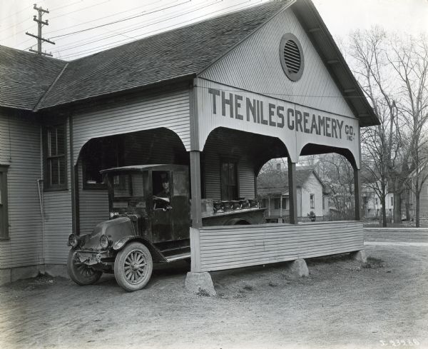 An International truck hauling pails of milk pulls out from underneath a covered entrance at The Niles Creamery Co. Inc. The truck is likely a model H, or 21.
