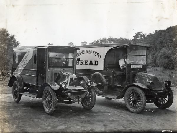 Two bakery trucks reading "American-Maid Bread," "...ansfield Bakery," and "New England Bakery Co." are parked side by side in a paved lot.