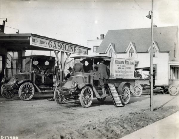 Men with International trucks from a caravan bound for Chicago from International Harvester's Akron Works in Ohio stop to fuel up at a Red Crown gasoline station. The text on the truck reads: "International Motor Trucks from the Factory, Akron, Ohio to Chicago; International Harvester Company of America Incorporated; Highway Deliveries Relieve Railroad Congestion."