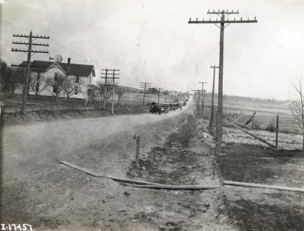 A caravan of trucks en route from International Harvester's Akron Works factory in Ohio to Chicago is traveling down a rural road lined with telephone poles.