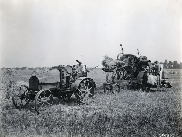 Two farmers use an International 8-16 tractor and a threshing machine in a field.