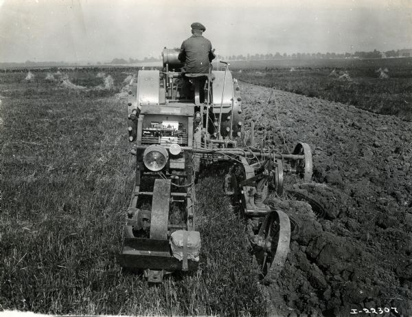 Rear view of a farmer using an International 8-16(?) tractor to plow a field.