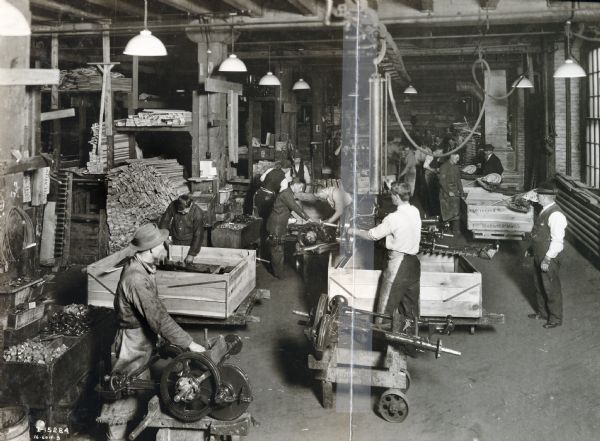 Factory workers assemble parts at International Harvester's McCormick Works. A large pile of wooden boards is in the background.