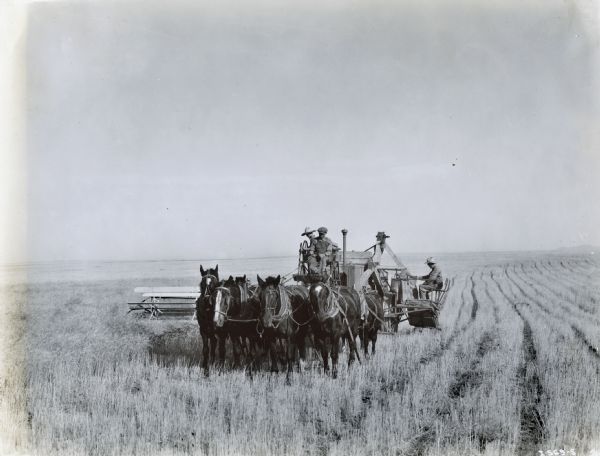 Farmers are leading a team of horses pulling a harvester-thresher (combine) through a field.