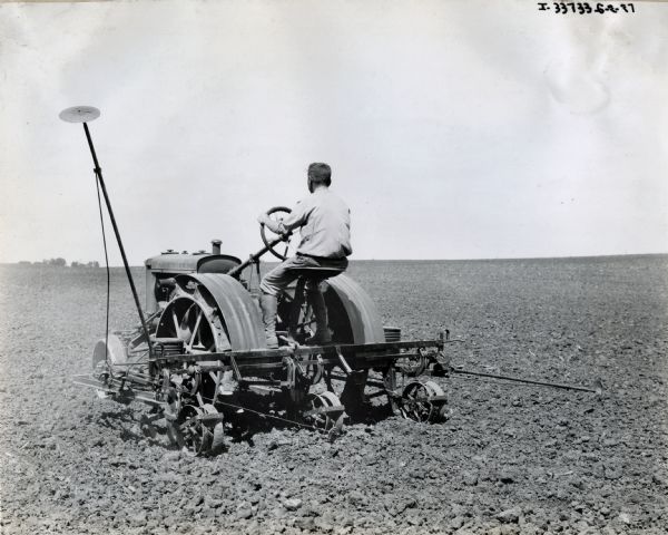 A man is operating a John Deere tractor with an attachment through a field. The handwritten text below the photograph identifies either the tractor or the attachment as being "experimental."