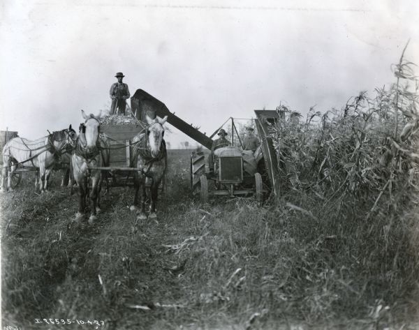Farmers operate a tractor, a Ronning ensilage cutter and a horse-drawn wagon in a field.